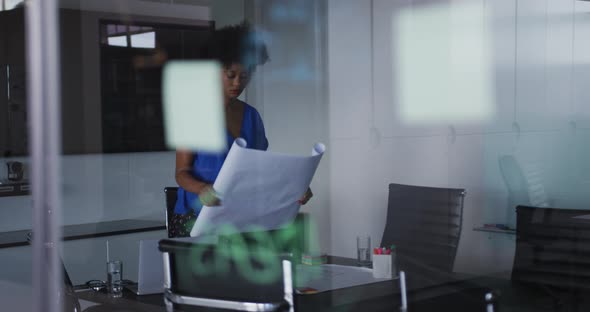 African american businesswoman unrolling technical drawing on table in meeting room