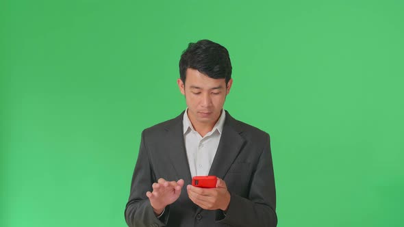 Happy Young Asian Business Man Use Mobile Phone While Standing On Green Screen In The Studio