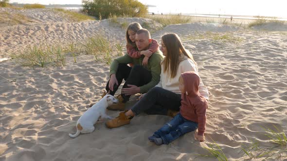 Family with a Son and Daughter and a Dog Sit on the Sand