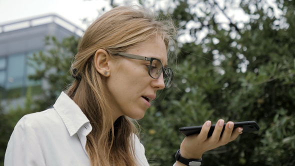Woman Wearing Glasses Using a Smart Phone Voice Recognition