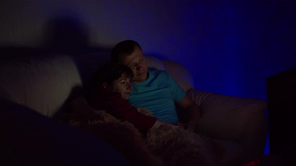 Married Couple Sitting Embracing Late at Night and Watching TV While Sitting on the Couch