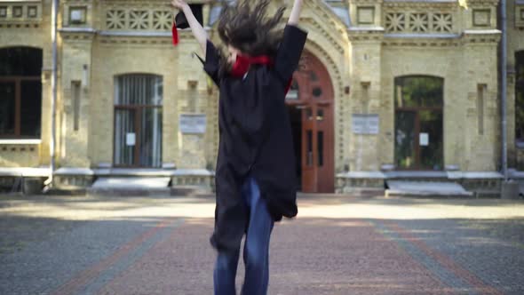 Excited Satisfied Beautiful Woman in Graduation Toga Jumping Rejoicing Looking at Camera Smiling