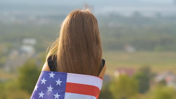 Young Pretty American Woman with Long Hair Holding Waving on Wind USA Flag on Her Sholders Standing