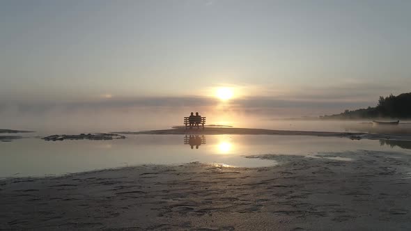 Couple in Love Sitting on a Bench in the Middle of the Lake and Meet the Sunrise