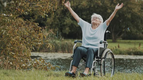 Senior Woman in the Wheelchair Outstretching Her Hands Near the River