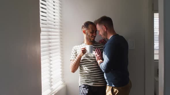 Multi ethnic gay male couple embracing and drinking coffee