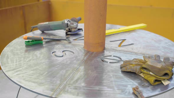 Dirty Gloves, Angle Grinder and Level Tool On Round Metal Table with Carved Letters. - close up