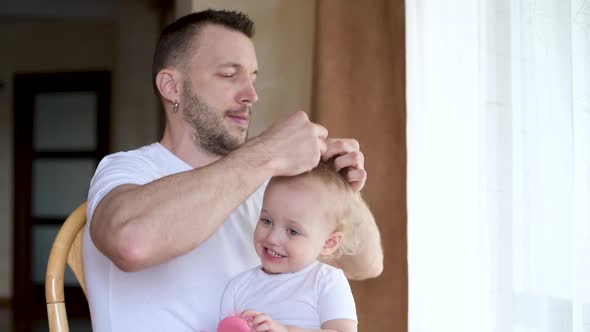 Father and little daughter have fun together. Dad does a hairstyle to daughter