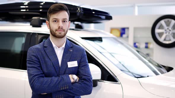Portrait of Young Car Salesman at Car Showroom Standing with Crossed Arms