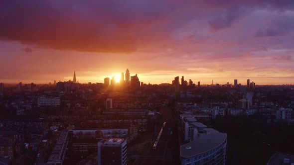 Aerial drone shot towards city of London skyscrapers as train passes underneath sunset