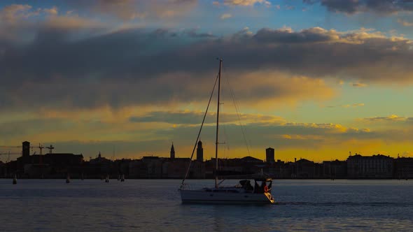 Yacht with Folded Sail Drifts on Lagoon Past Historic City