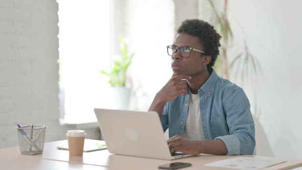 Young African Man Thinking While Working on Laptop in Office