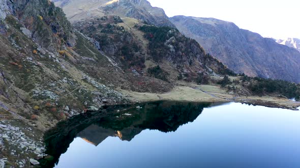 Lac d'Espingo reflecting mountain lake located in Haute-Garonne, Pyrénées, France, Aerial flyover pa