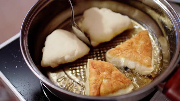 a Woman's Hand Turns Over Pies That are Fried in Boiling Oil