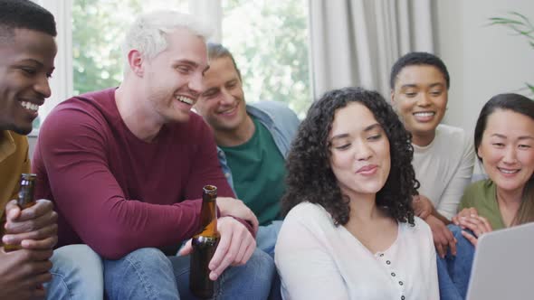 Diverse group of happy male and female friends looking at laptop and laughing in living room