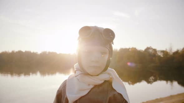 Little Aviator Boy in Retro Pilot Costume with Scarf and Glasses Looking at Camera Smiling at Sunset