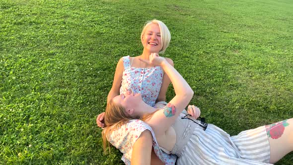 A Lesbian Couple in the Park Sit on the Grass and Laugh