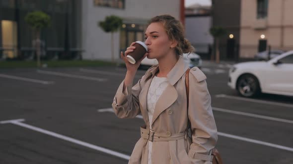 Woman in Trench Coat Walks Drinking Takeaway Coffee