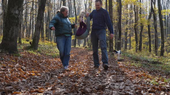 A man and a woman walk through the leaves in an autumn forest, holding hands with a child