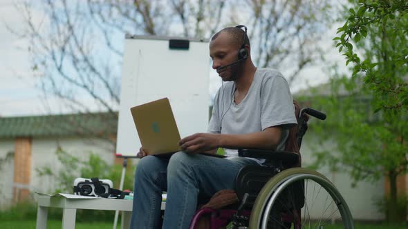 Portrait of Concentrated Serious Paralyzed Man in Wheelchair Talking at Laptop Web Camera