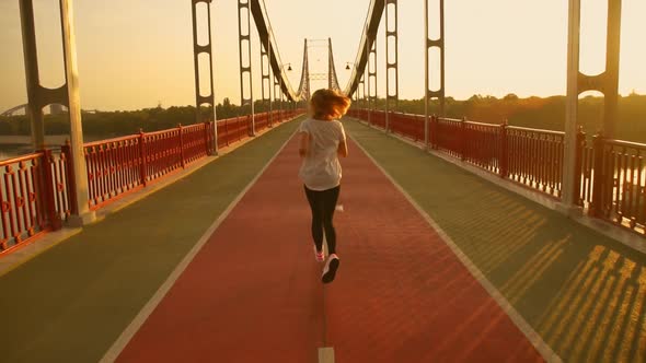 Back View of a Woman Running Along the Bridge