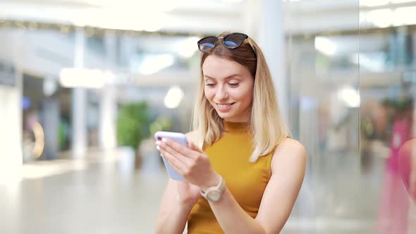 Young woman consumer in the mall browses chat and uses using a smartphone.