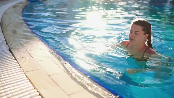 Woman Swims in the Pool with Blue Transparent Water in the Sunny Day Outdoors, Relaxing an Swimming