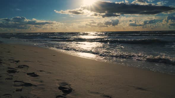 Sunset Behind Clouds Over Sea Waves and Sandy Beach