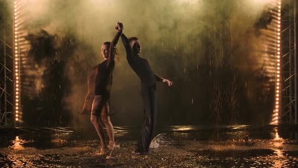 Attractive Man and Woman Gracefully Dance Jive in the Rain Puddles Under the Drops of Water. Smoky