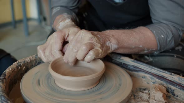 Close-up Shot of Potter's Hands Smoothing Molded Pot on Spinning Throwing Wheel in Studio