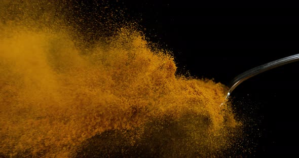 Spoon and Curry Powder falling against Black Background, Slow motion 4K