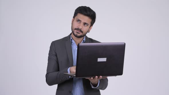 Young Happy Bearded Indian Businessman Thinking While Using Laptop