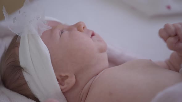 Side View Crying Newborn Baby Girl in White Hair Hoop Lying on Bed