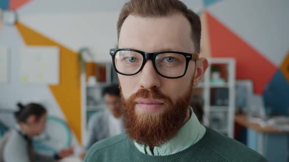 Close-up Portrait of Bearded Young Man in Glasses Looking at Camera in Office