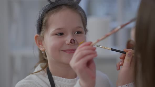 Headshot Portrait of Little Caucasian Girl Smiling Painting Face with Sister at Home