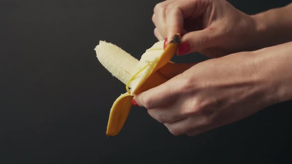Girl sexually peels a banana close-up. Juicy and ripe fruit on a dark background 