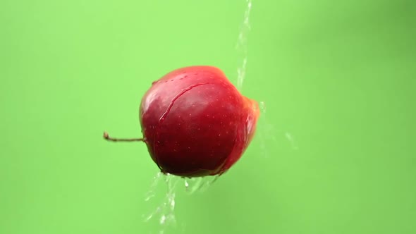 A Jet of Water Pours on a Ripe Red Apple Spinning on a Green Background
