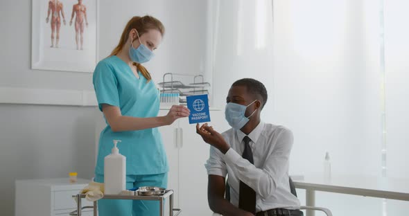 Nurse in Safety Mask Give Vaccine Certificate to Vaccinated African Businessman
