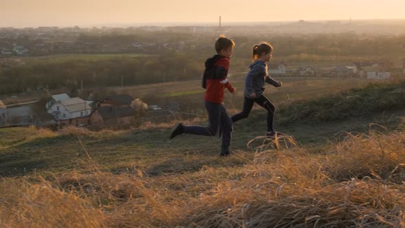 Two children boy and girl running together outdoors on a summer field at sunset alt