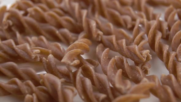 Whole grain spiral pasta fusilli falling on a white plate in slow motion