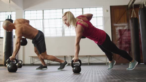 Fit caucasian woman and man working out with kettle bells at the gym