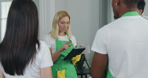 Woman in Uniform from Cleaning Service Holding in Her Hands Tablet PC and Giving Instructions