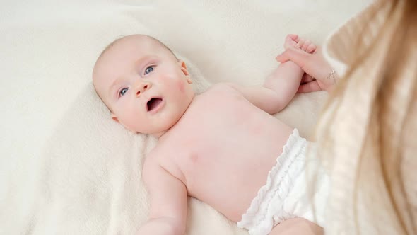 Mother Making Massage and Gymnastics to Her Little Baby Boy Lying on Bed