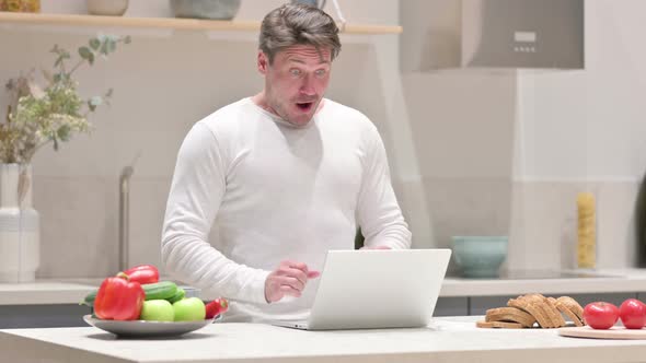 Middle Aged Man Celebrating Success While Using Laptop in Kitchen