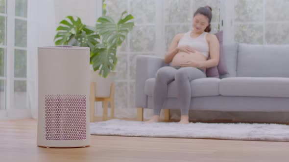 air purifier in living room for clean dust and fresh air with pregnant woman sitting on couch