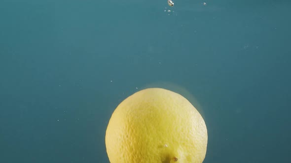 Falling Lemon Into Splashing Water on Blue Background