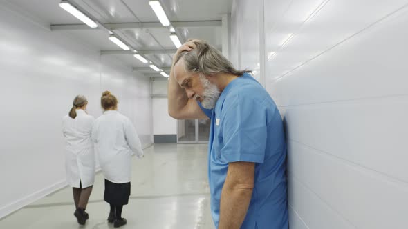 Stressed Tired Aged Surgeon Leaning on Wall in Hospital Corridor After Difficult Surgery