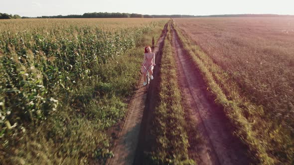 A Girl on a Bicycle is Riding a Field Road at Sunset