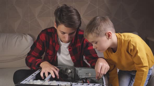 Young Man Teenager Shows His Younger Brother What Is Inside the Computer