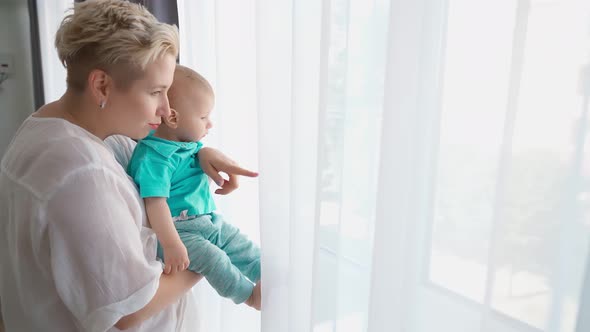 Positive Woman Hugging and Kissing Little Son Near Window
